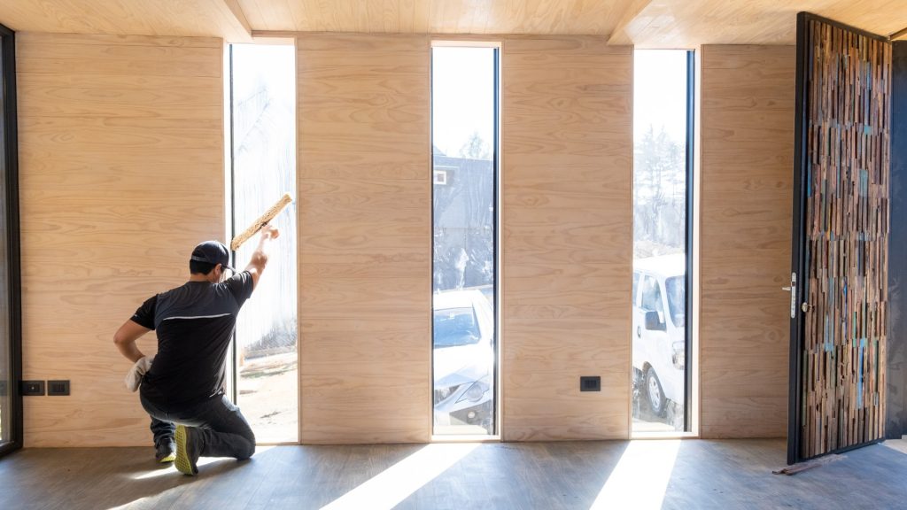 Worker performing residential window cleaning on tall narrow windows inside a modern home.